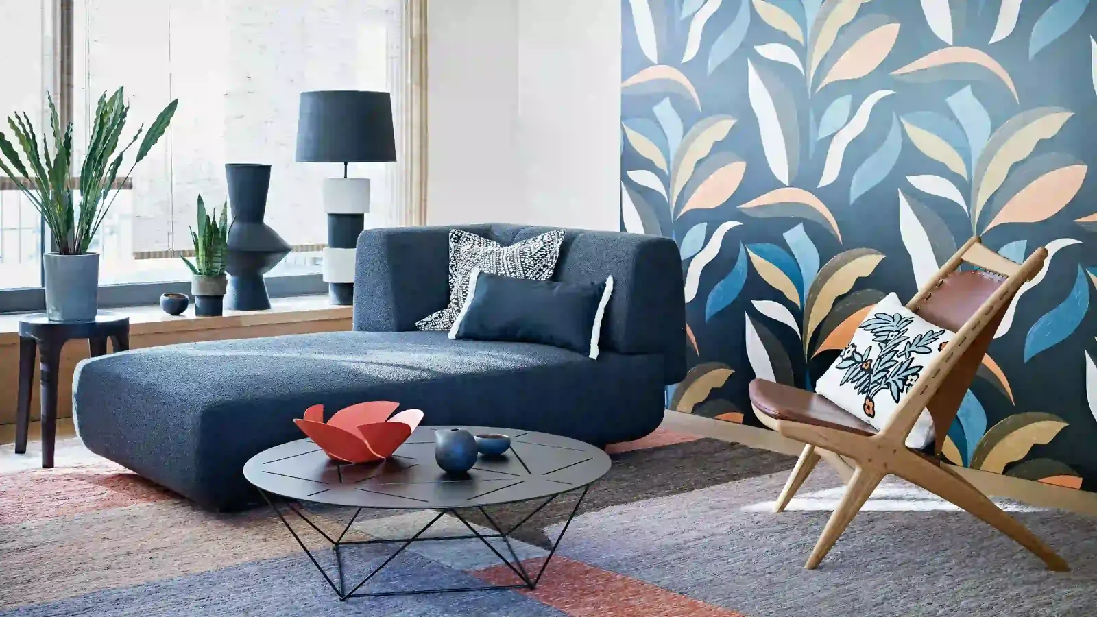 Living room with large-scale painted leaf wallpaper behind a navy sofa and a wood-framed chair