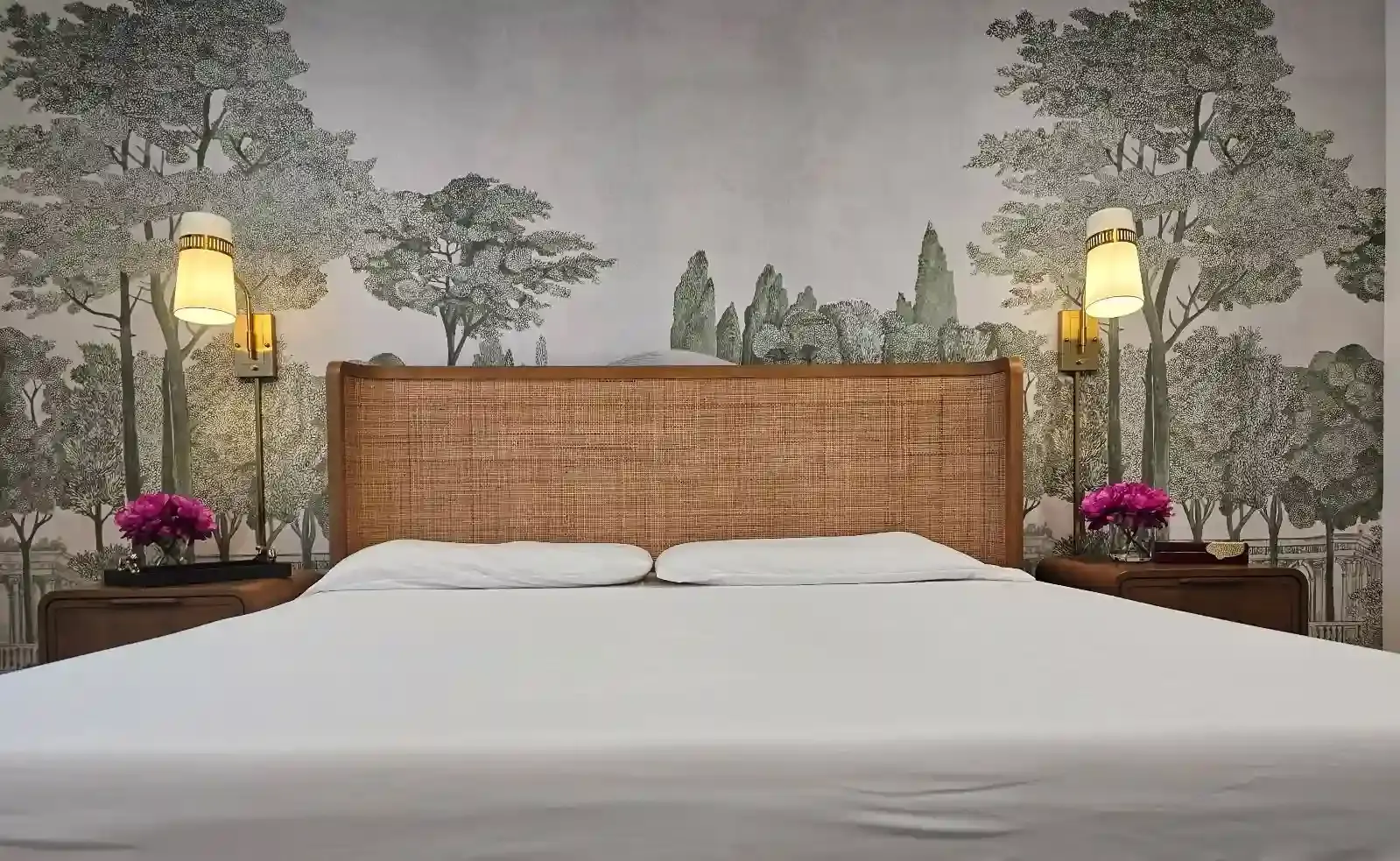 Bedroom wall covered in a pale scenic mural of trees behind a cane headboard